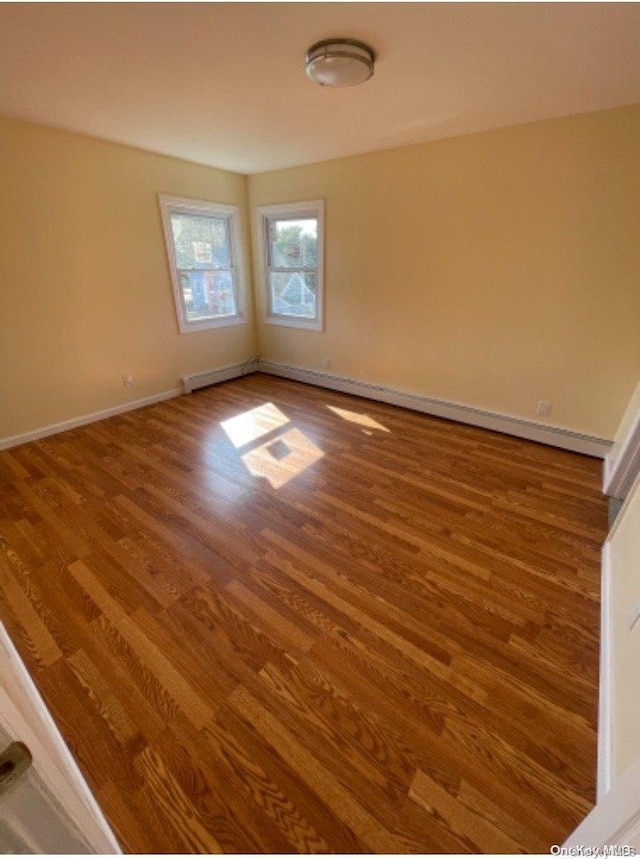 empty room with wood-type flooring and a baseboard heating unit