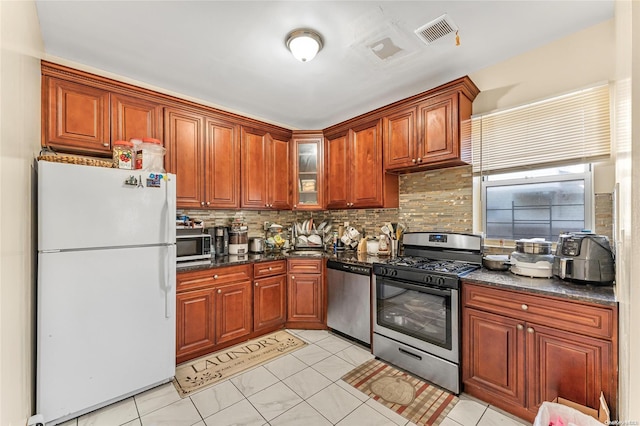 kitchen with decorative backsplash, light tile patterned floors, stainless steel appliances, and dark stone counters