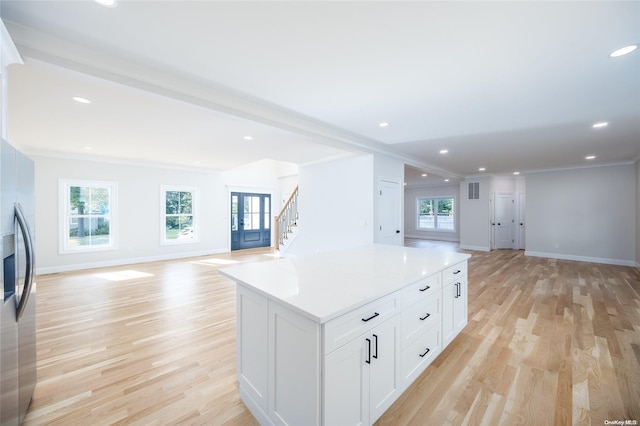 kitchen featuring white cabinetry, a center island, light hardwood / wood-style flooring, stainless steel fridge, and ornamental molding