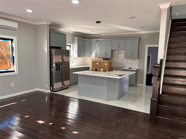 kitchen featuring gray cabinetry, stainless steel fridge, crown molding, and a kitchen island with sink