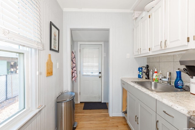 kitchen with light wood-type flooring, tasteful backsplash, exhaust hood, sink, and white cabinetry