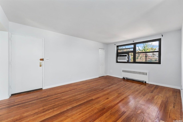 unfurnished room featuring radiator heating unit, hardwood / wood-style flooring, and cooling unit