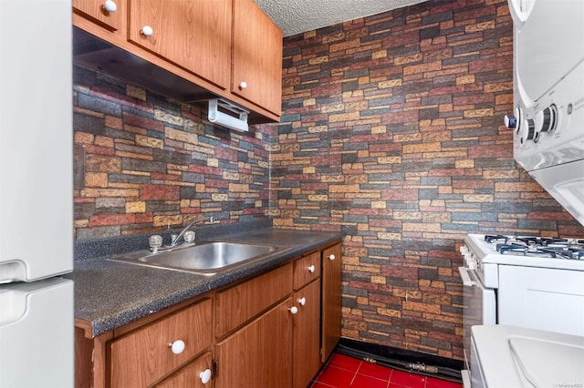 kitchen with a textured ceiling, white appliances, dark tile patterned floors, and sink