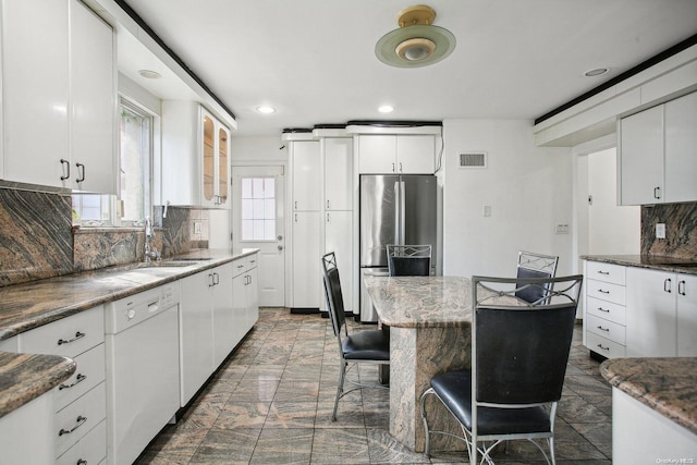 kitchen with dishwasher, decorative backsplash, stainless steel fridge, dark stone countertops, and white cabinetry