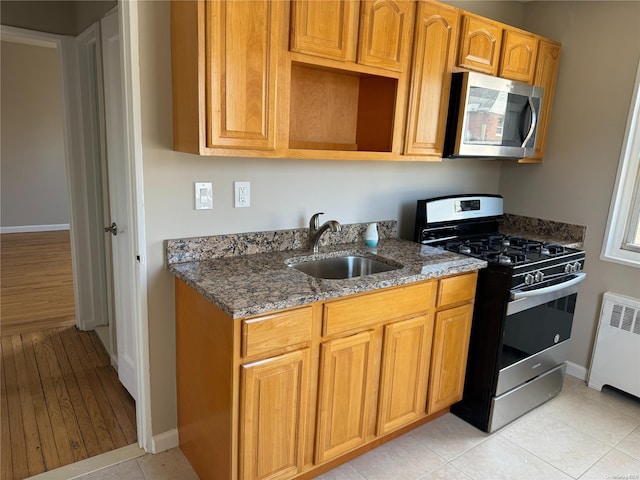 kitchen featuring radiator, sink, dark stone counters, appliances with stainless steel finishes, and light wood-type flooring