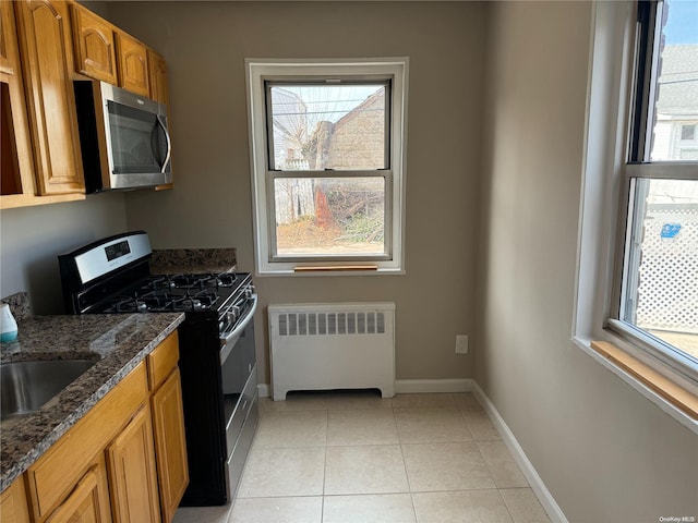 kitchen with light tile patterned flooring, radiator heating unit, appliances with stainless steel finishes, and dark stone counters