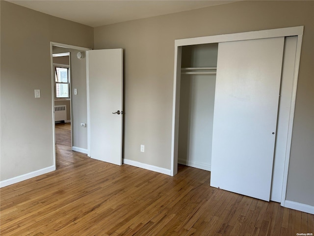 unfurnished bedroom with hardwood / wood-style floors, radiator, and a closet