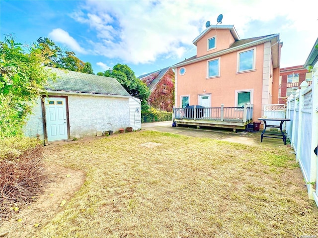 back of house with stucco siding, a wooden deck, fence, and a yard