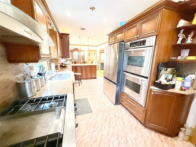 kitchen featuring appliances with stainless steel finishes, brown cabinetry, a sink, and pendant lighting