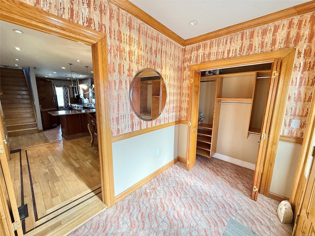 corridor featuring wallpapered walls, baseboards, wainscoting, stairs, and crown molding