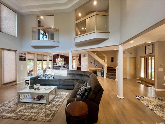 living room featuring decorative columns, baseboards, stairway, light wood-type flooring, and a chandelier