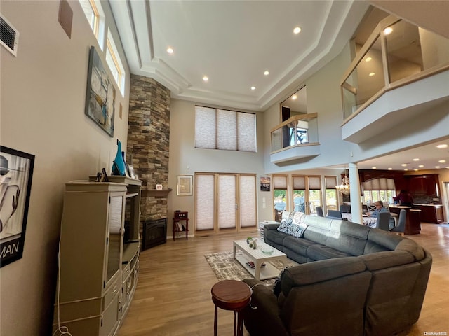 living area featuring a towering ceiling, light wood finished floors, recessed lighting, and a stone fireplace