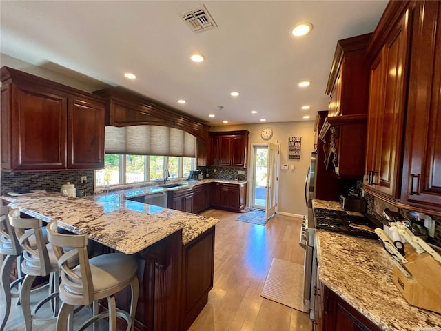 kitchen with visible vents, light wood-style flooring, light stone countertops, a peninsula, and a kitchen bar