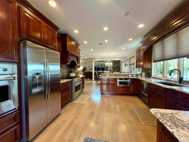 kitchen featuring pendant lighting, tasteful backsplash, appliances with stainless steel finishes, light wood-style floors, and a sink