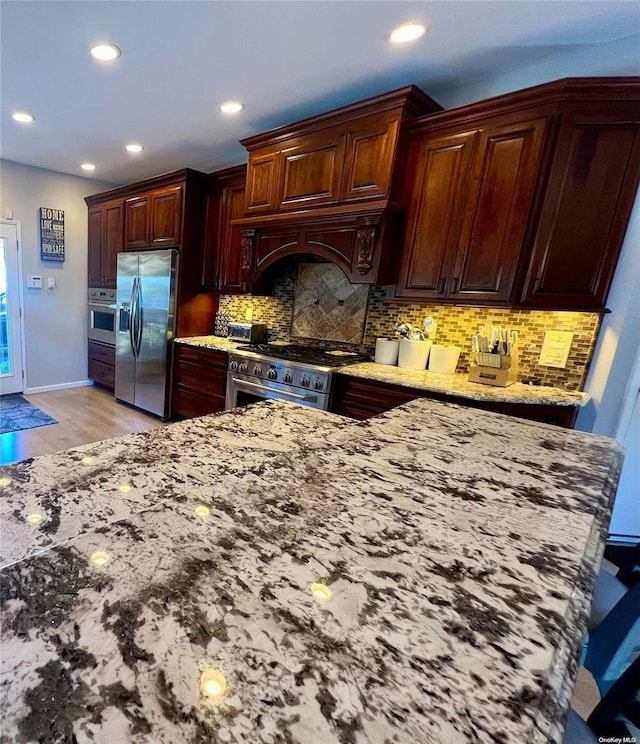 kitchen featuring light wood-type flooring, light stone counters, stainless steel appliances, and decorative backsplash