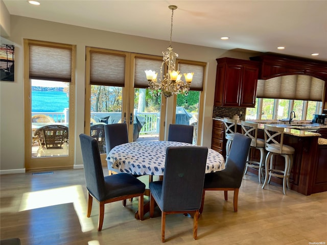 dining room featuring baseboards, a water view, an inviting chandelier, light wood-style floors, and recessed lighting