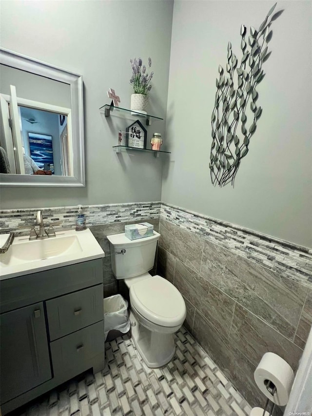 bathroom with toilet, wainscoting, tile walls, and vanity