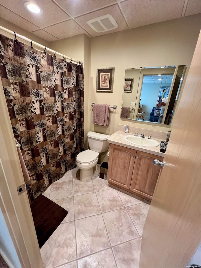 bathroom with a paneled ceiling, visible vents, toilet, vanity, and tile patterned floors