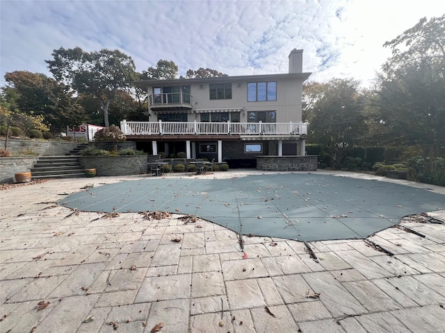 rear view of house with a patio, a chimney, a balcony, a covered pool, and stairs