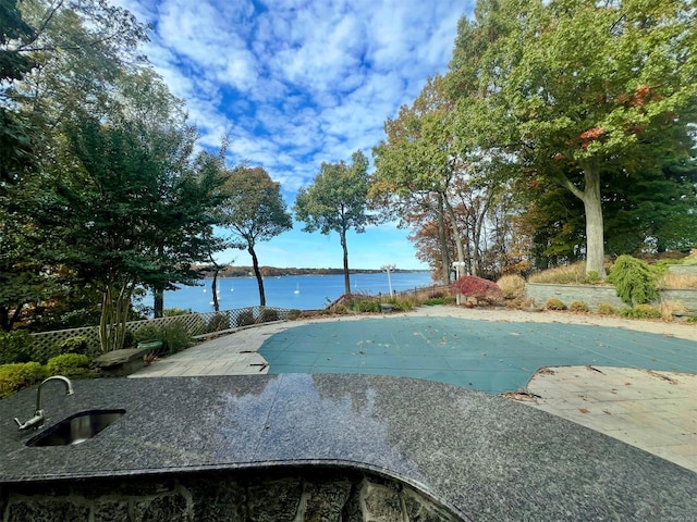 view of swimming pool featuring a water view, a covered pool, fence, and a patio