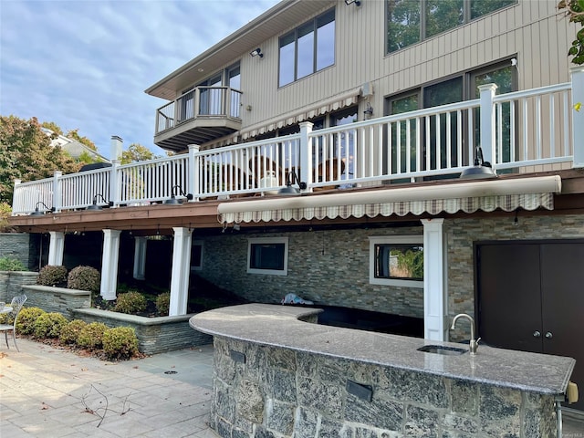 rear view of house with a balcony, a patio area, stone siding, and a sink