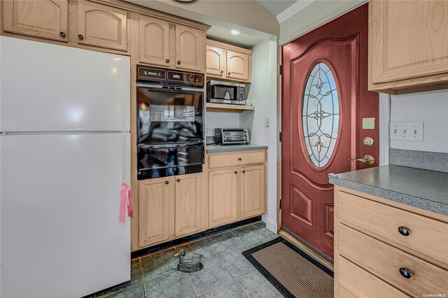 kitchen with white refrigerator, black double oven, light brown cabinetry, dark tile patterned flooring, and ornamental molding