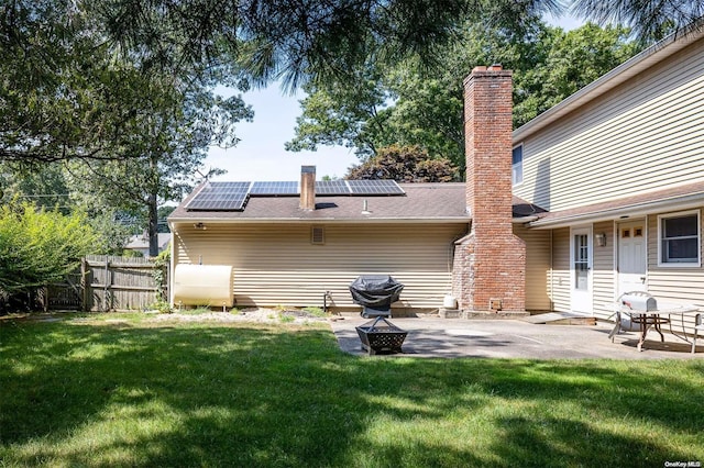 rear view of property featuring a fire pit, solar panels, a patio area, and a yard