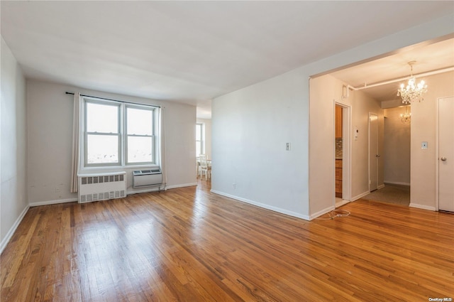 empty room featuring a wall mounted AC, radiator heating unit, a chandelier, and hardwood / wood-style flooring