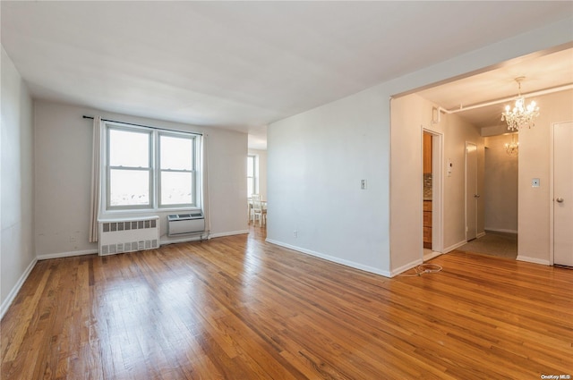 spare room featuring hardwood / wood-style flooring, a wall mounted AC, a notable chandelier, and radiator