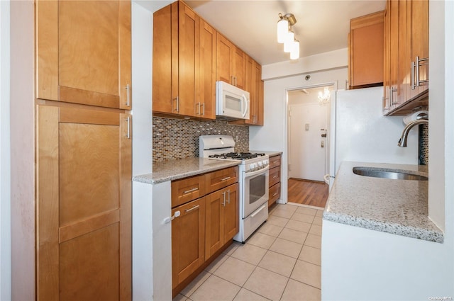 kitchen with white appliances, light stone counters, light tile patterned floors, tasteful backsplash, and sink