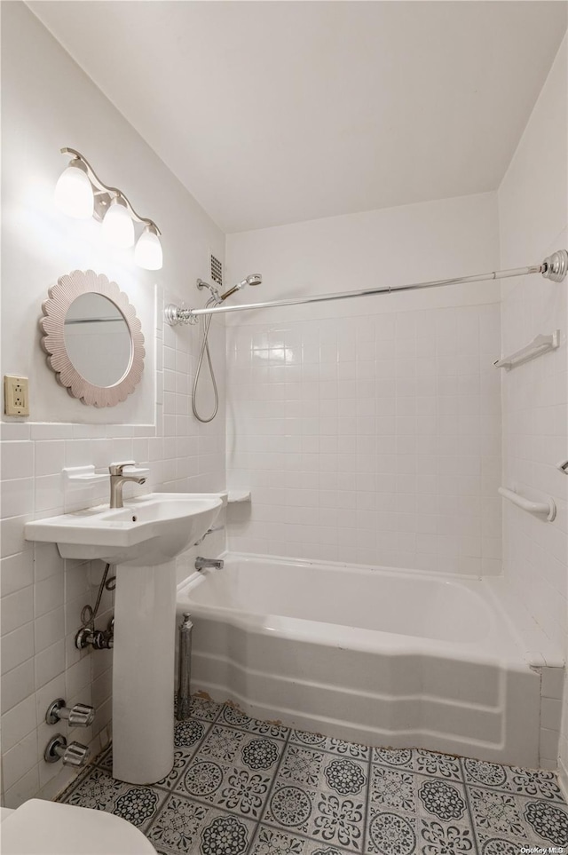 bathroom featuring toilet, tile patterned floors, tile walls, and tiled shower / bath