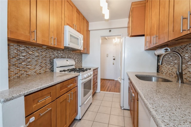 kitchen featuring light tile patterned flooring, sink, decorative backsplash, light stone countertops, and white appliances