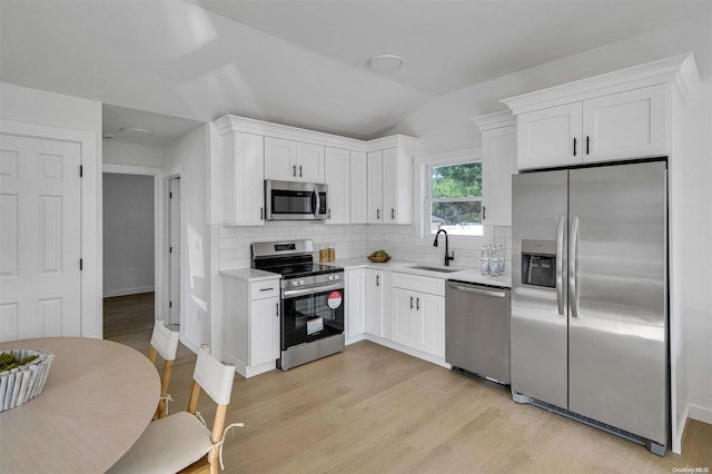 kitchen with lofted ceiling, backsplash, sink, appliances with stainless steel finishes, and white cabinetry