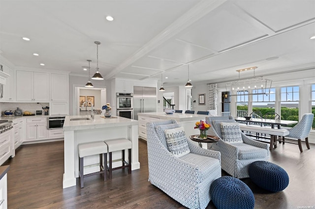 interior space with appliances with stainless steel finishes, white cabinetry, a kitchen island with sink, and pendant lighting