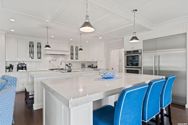 kitchen featuring stainless steel appliances, dark wood-type flooring, decorative light fixtures, white cabinets, and a large island