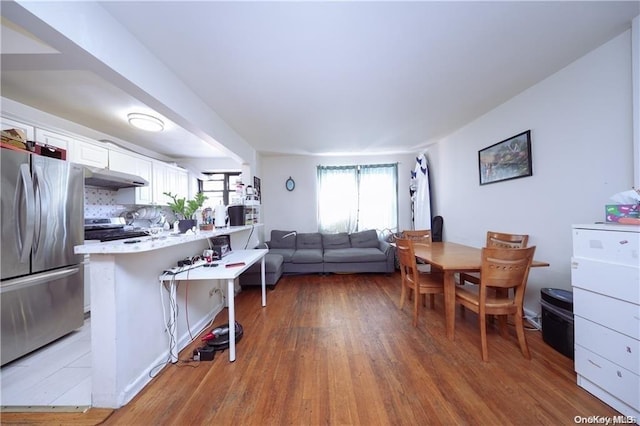 kitchen with kitchen peninsula, hardwood / wood-style flooring, appliances with stainless steel finishes, a kitchen bar, and white cabinetry