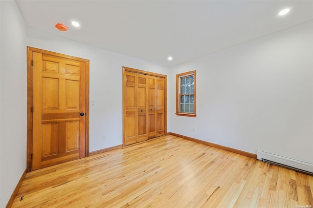 unfurnished bedroom with baseboard heating, a closet, and light wood-type flooring