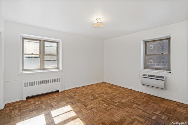 empty room featuring a wall unit AC, radiator, and dark parquet flooring