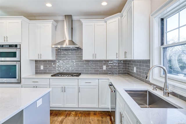 kitchen featuring white cabinetry, sink, stainless steel appliances, wall chimney range hood, and backsplash