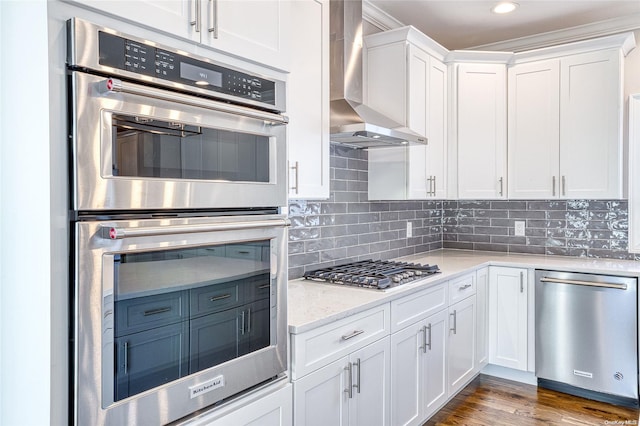 kitchen featuring wall chimney range hood, light stone counters, appliances with stainless steel finishes, dark hardwood / wood-style flooring, and white cabinetry