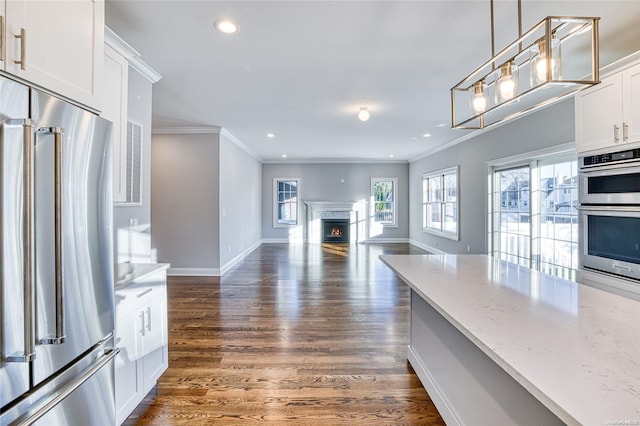 kitchen with dark wood-type flooring, light stone counters, decorative light fixtures, white cabinets, and appliances with stainless steel finishes