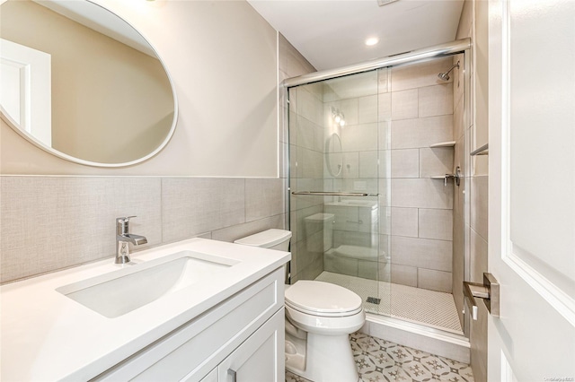 bathroom with a shower with door, vanity, tile walls, and toilet