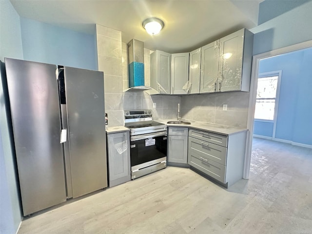 kitchen featuring a sink, appliances with stainless steel finishes, gray cabinets, decorative backsplash, and wall chimney exhaust hood