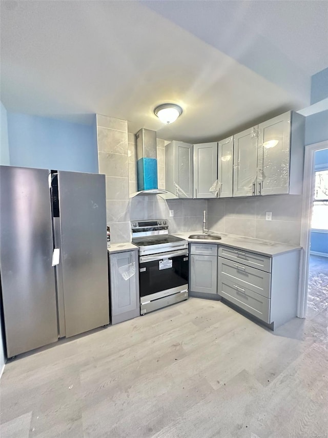 kitchen featuring stainless steel appliances, tasteful backsplash, gray cabinetry, a sink, and wall chimney range hood