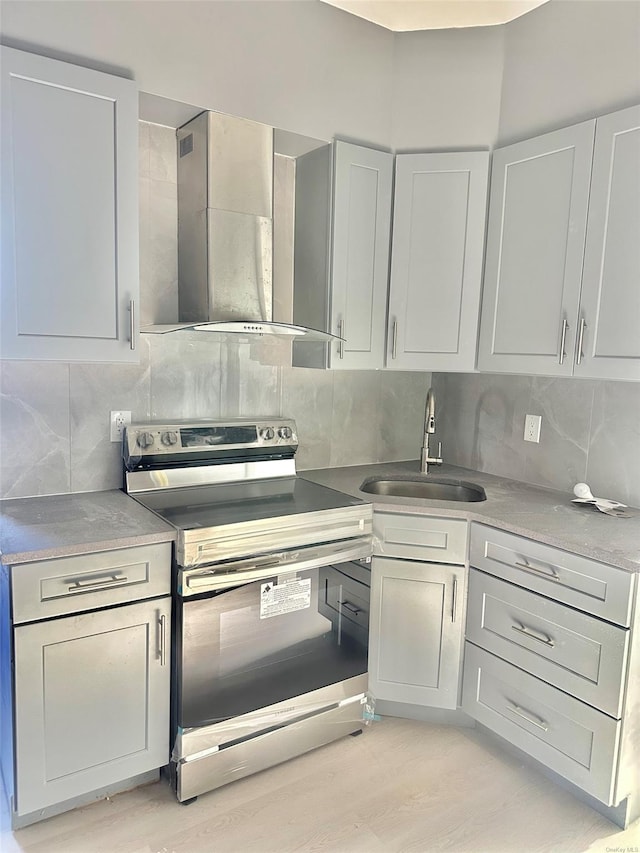 kitchen featuring tasteful backsplash, light wood-style floors, stainless steel range with electric cooktop, wall chimney range hood, and a sink