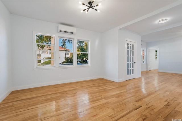 unfurnished room featuring an AC wall unit, light hardwood / wood-style flooring, and an inviting chandelier