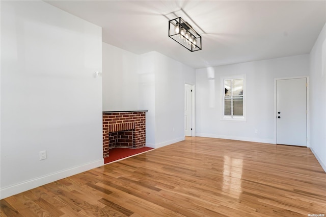 unfurnished living room with a brick fireplace, an inviting chandelier, and light hardwood / wood-style flooring