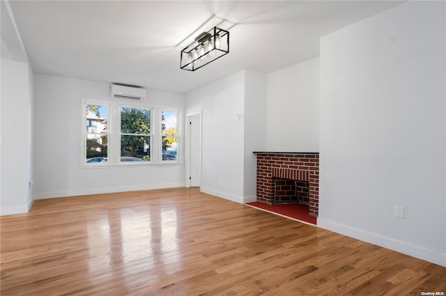 unfurnished living room featuring a brick fireplace, light hardwood / wood-style floors, and an AC wall unit