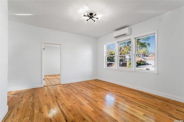 spare room featuring an inviting chandelier, a wall unit AC, and light hardwood / wood-style flooring