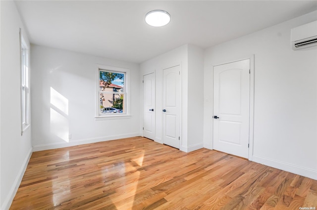 unfurnished bedroom featuring a wall mounted air conditioner, two closets, and light hardwood / wood-style flooring